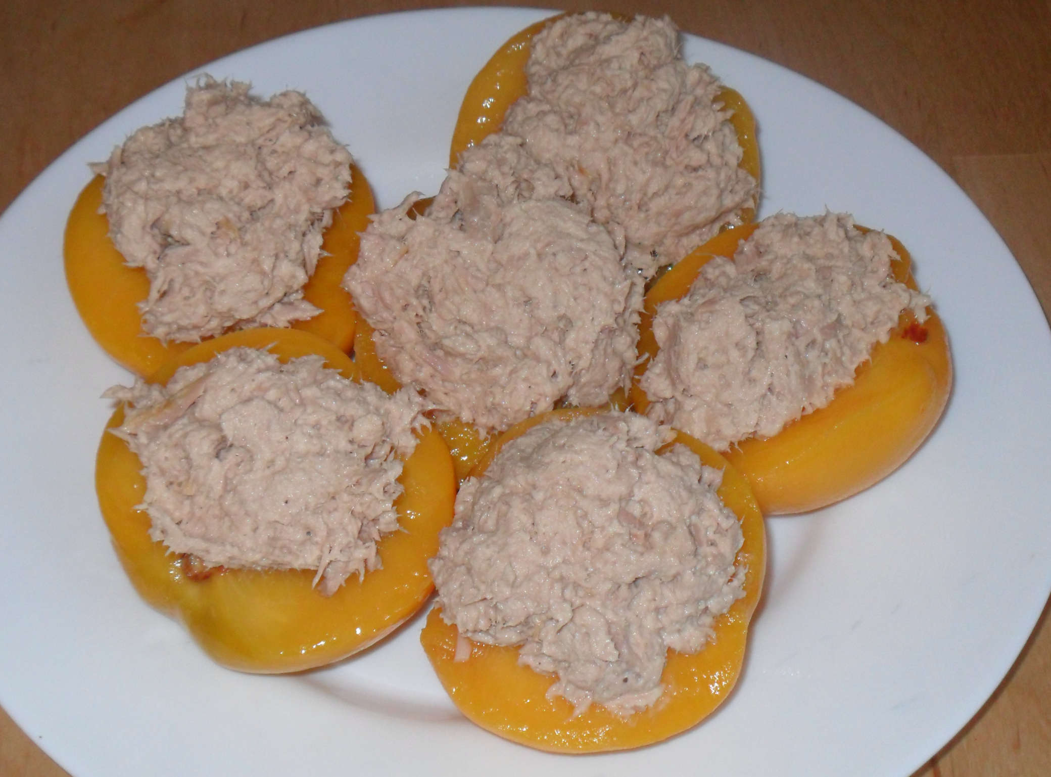 
    A white plate containing six peach halves, each dolloped with a small pile of what looks like grey mush.